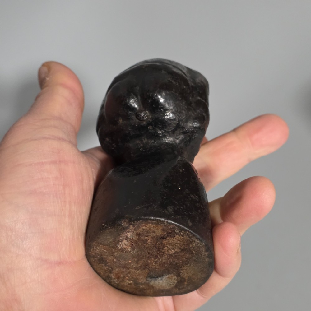 A nineteenth-century dark cast iron paperweight shaped as a crouching male figure in a hat set upon a cylindrical pedestal. View III