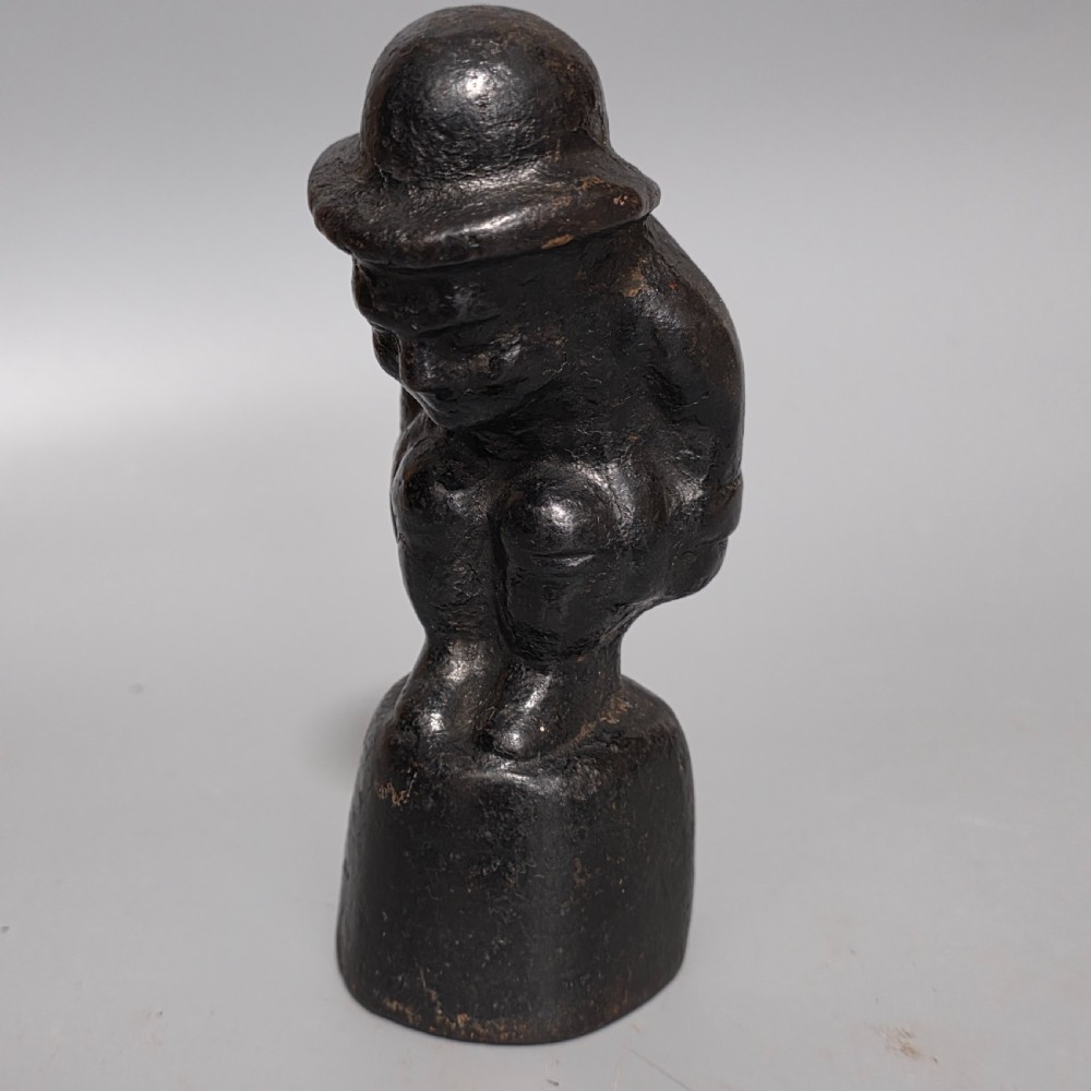 A nineteenth-century dark cast iron paperweight shaped as a crouching male figure in a hat set upon a cylindrical pedestal. View IV