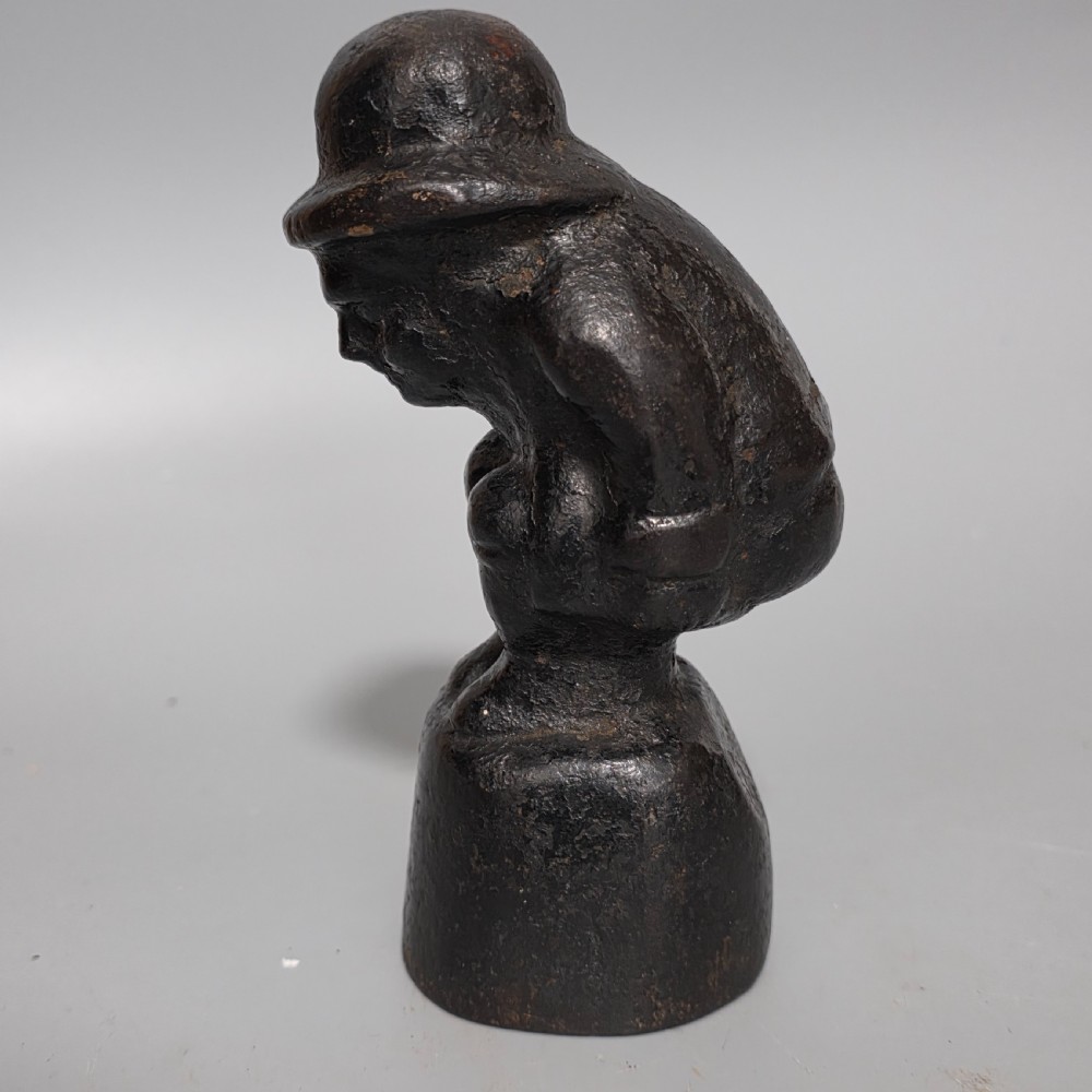 A nineteenth-century dark cast iron paperweight shaped as a crouching male figure in a hat set upon a cylindrical pedestal. View VI