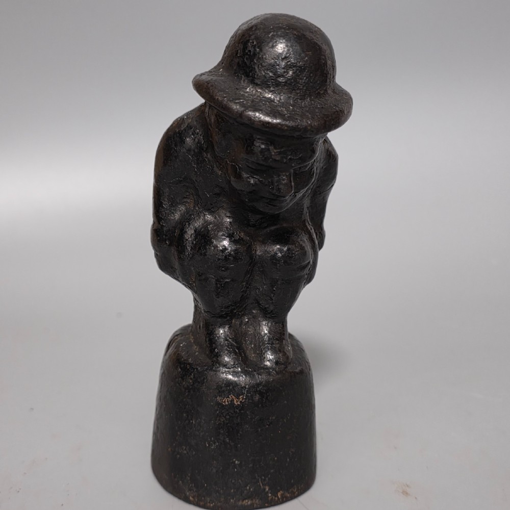 A nineteenth-century dark cast iron paperweight shaped as a crouching male figure in a hat set upon a cylindrical pedestal. View IX