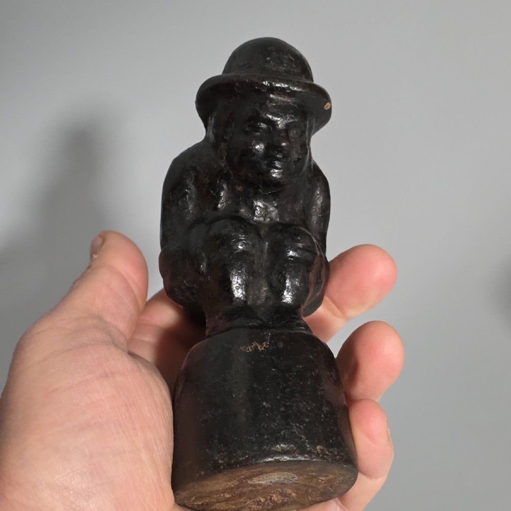 A nineteenth-century dark cast iron paperweight shaped as a crouching male figure in a hat set upon a cylindrical pedestal. View XII