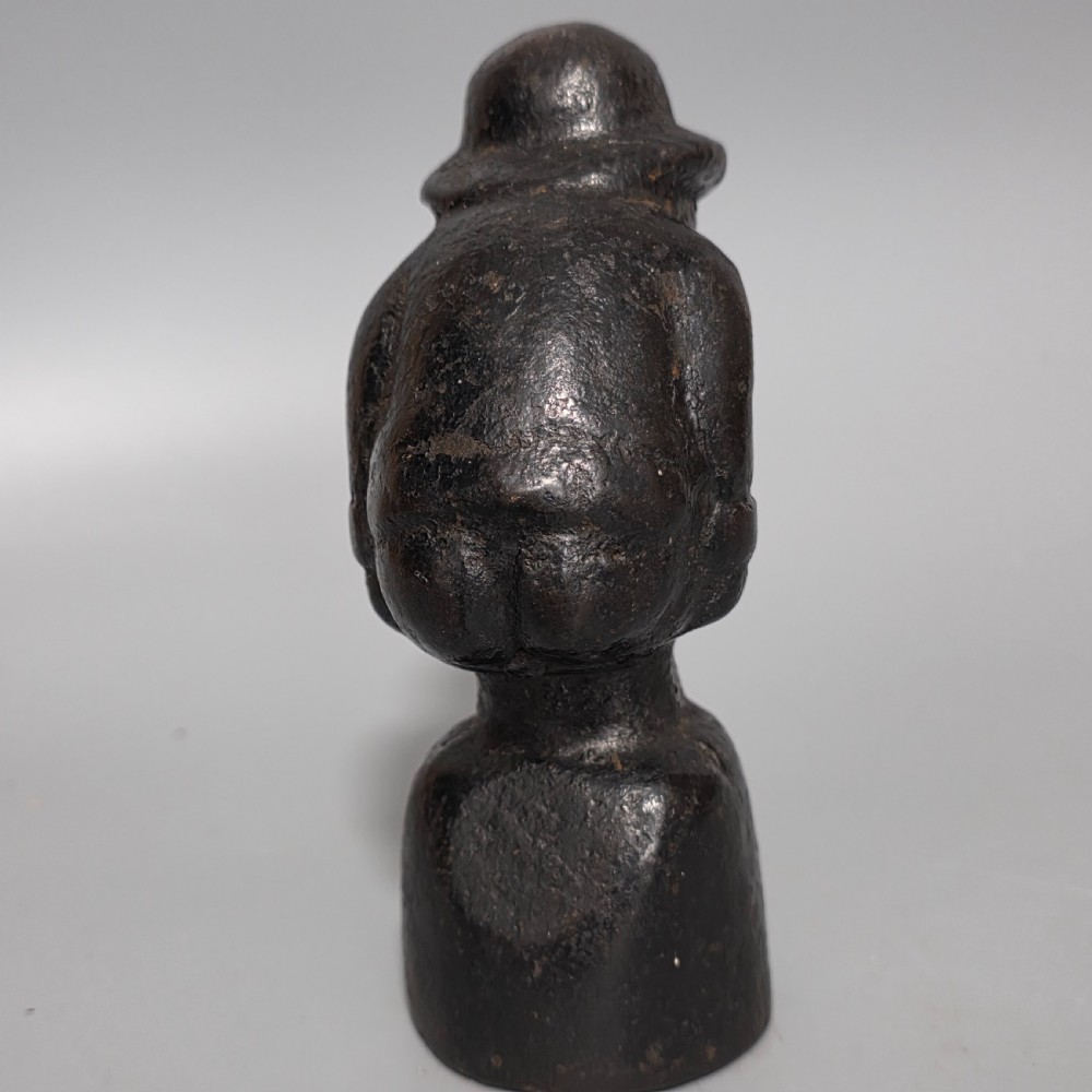 A nineteenth-century dark cast iron paperweight shaped as a crouching male figure in a hat set upon a cylindrical pedestal. View XIV
