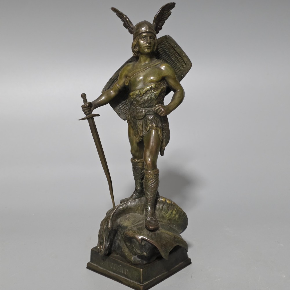 A patinated bronze sculpture depicting the mythical hero Siegfried standing victorious with a sword, winged helmet, and shield above a dragon base.
