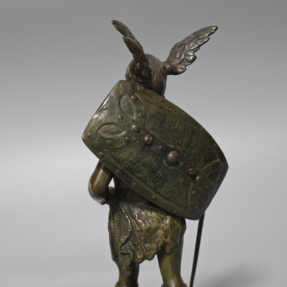A patinated bronze sculpture depicting the mythical hero Siegfried standing victorious with a sword, winged helmet, and shield above a dragon base. View IV