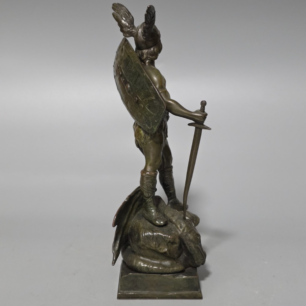 A patinated bronze sculpture depicting the mythical hero Siegfried standing victorious with a sword, winged helmet, and shield above a dragon base. View V