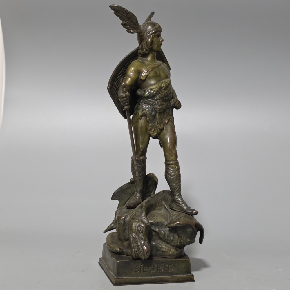 A patinated bronze sculpture depicting the mythical hero Siegfried standing victorious with a sword, winged helmet, and shield above a dragon base. View VI