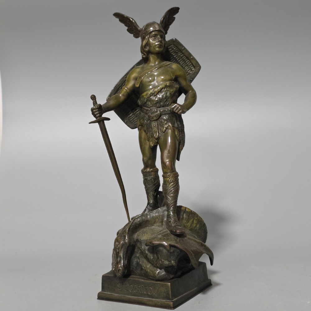A patinated bronze sculpture depicting the mythical hero Siegfried standing victorious with a sword, winged helmet, and shield above a dragon base. View VII