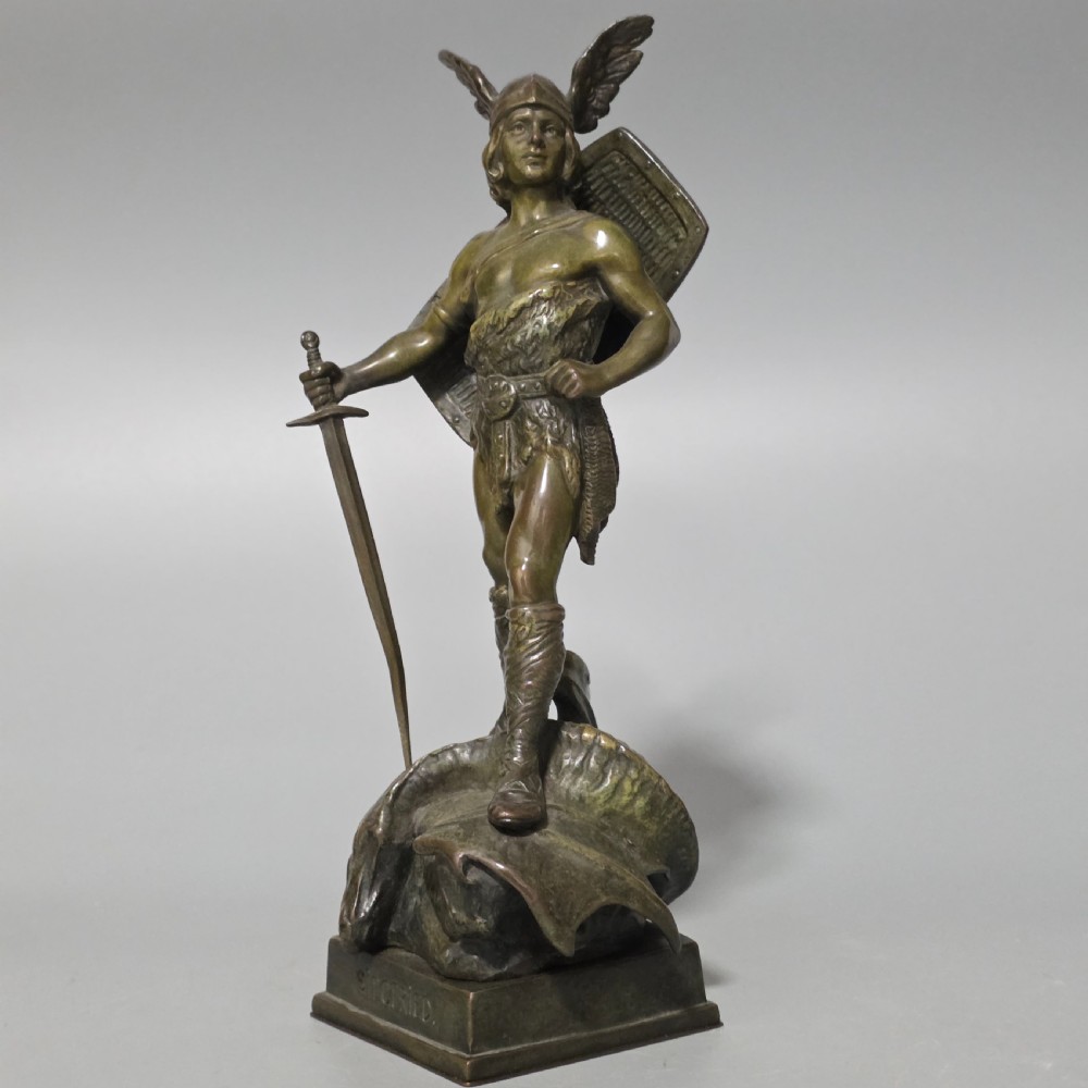 A patinated bronze sculpture depicting the mythical hero Siegfried standing victorious with a sword, winged helmet, and shield above a dragon base. View VIII