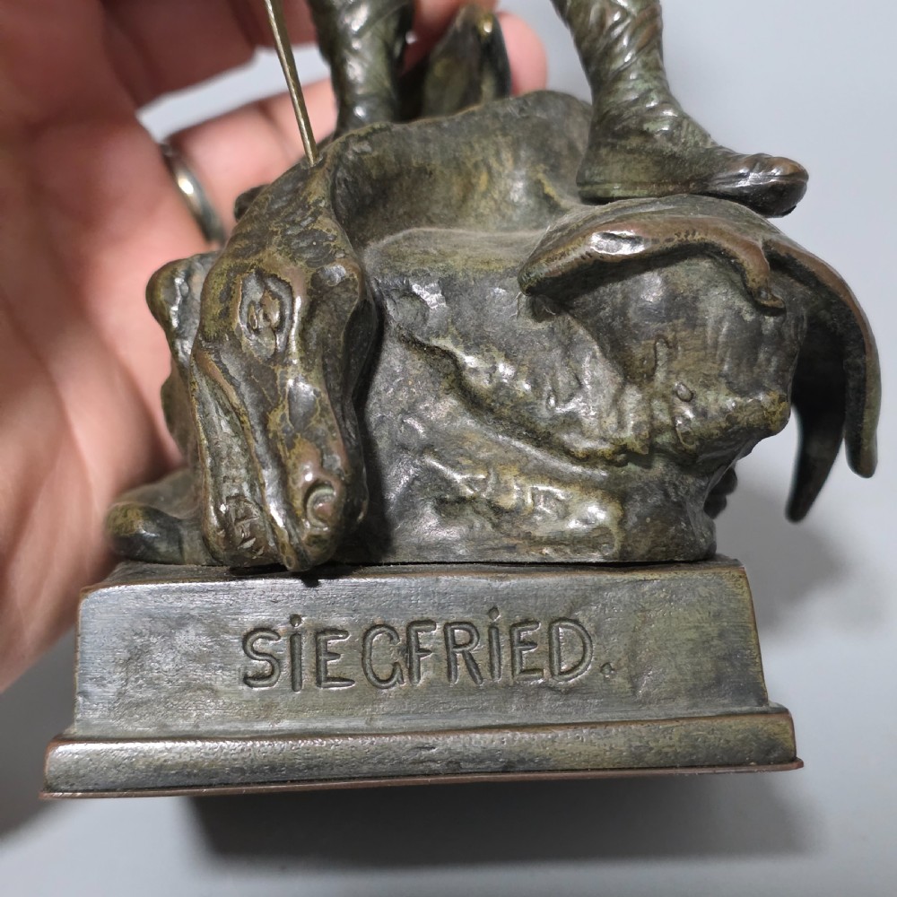 A patinated bronze sculpture depicting the mythical hero Siegfried standing victorious with a sword, winged helmet, and shield above a dragon base. View XV