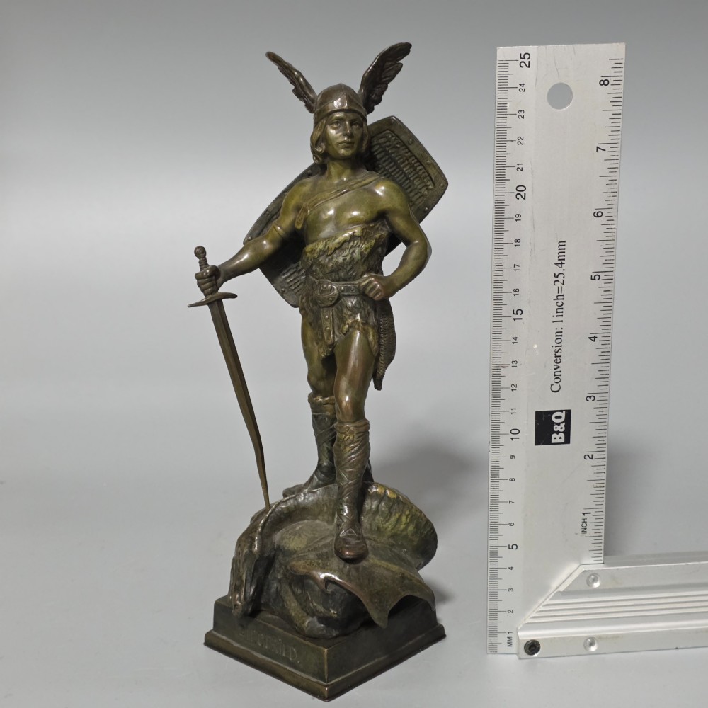 A patinated bronze sculpture depicting the mythical hero Siegfried standing victorious with a sword, winged helmet, and shield above a dragon base. View XVI