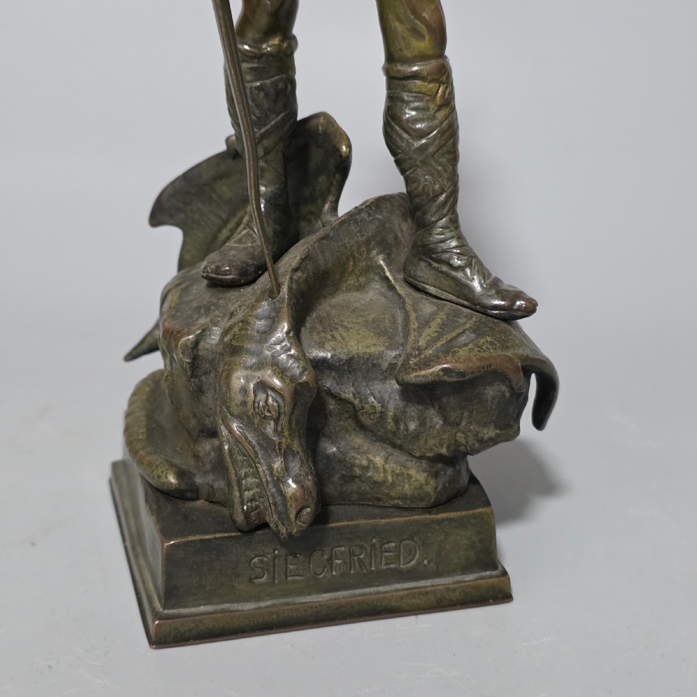 A patinated bronze sculpture depicting the mythical hero Siegfried standing victorious with a sword, winged helmet, and shield above a dragon base. View XX