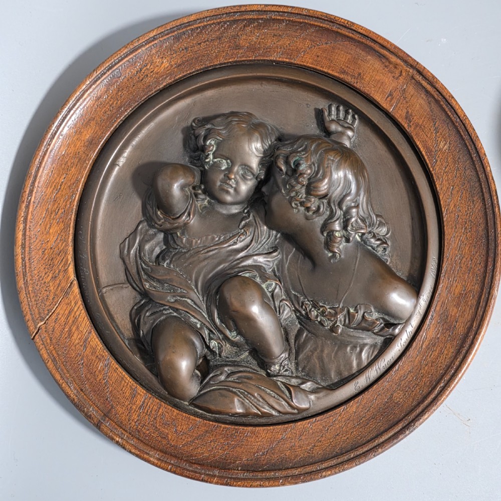 A circular Victorian bronze relief plaque depicting two young children in high relief, housed within a turned oak frame.