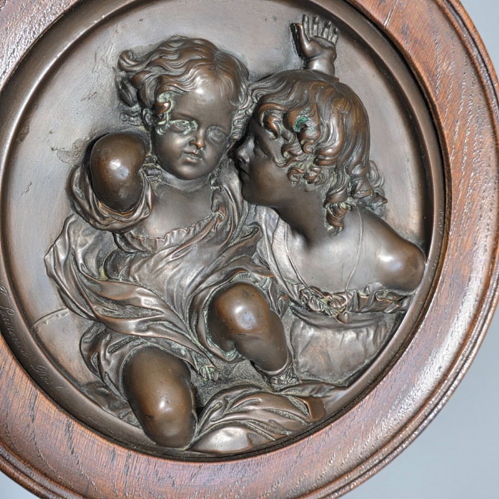 A circular Victorian bronze relief plaque depicting two young children in high relief, housed within a turned oak frame. View II