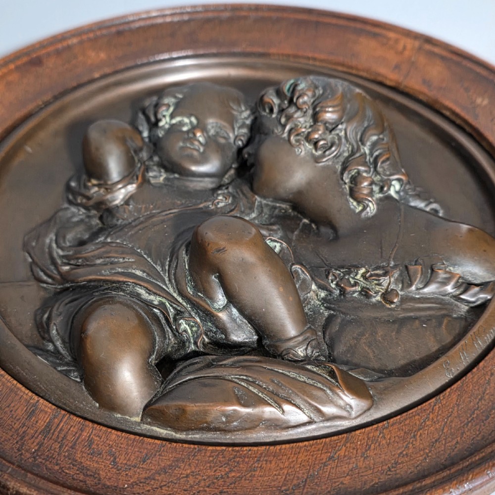 A circular Victorian bronze relief plaque depicting two young children in high relief, housed within a turned oak frame. View III