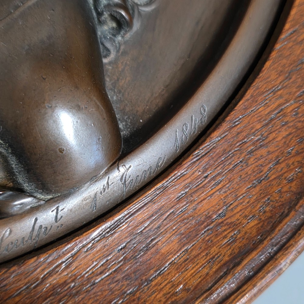 A circular Victorian bronze relief plaque depicting two young children in high relief, housed within a turned oak frame. View VII