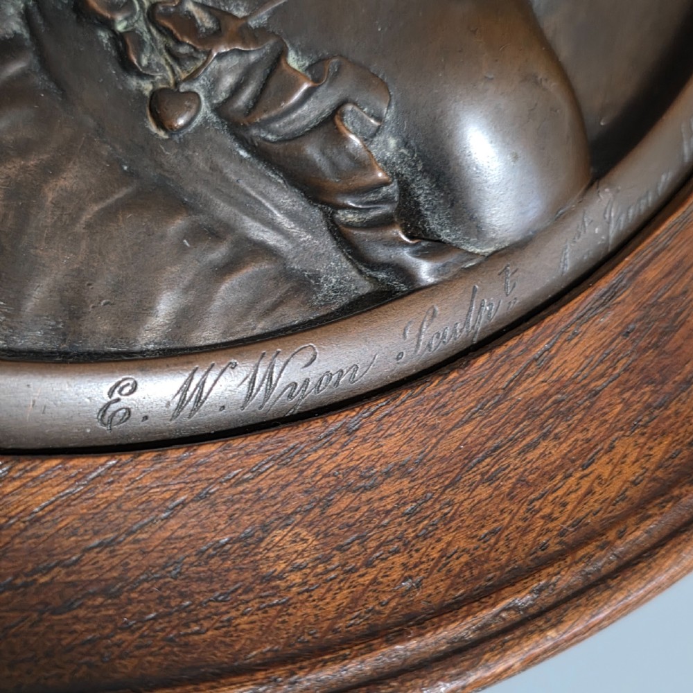 A circular Victorian bronze relief plaque depicting two young children in high relief, housed within a turned oak frame. View VIII