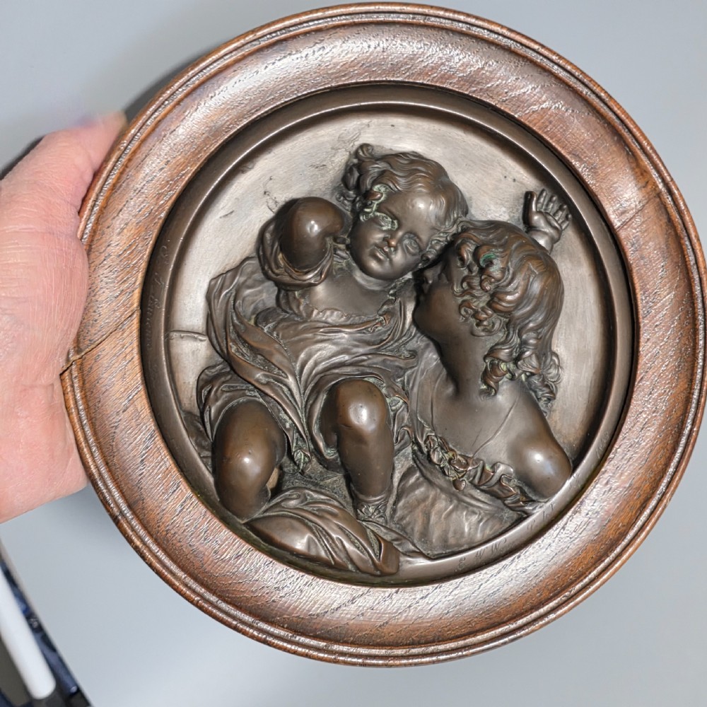 A circular Victorian bronze relief plaque depicting two young children in high relief, housed within a turned oak frame. View IX