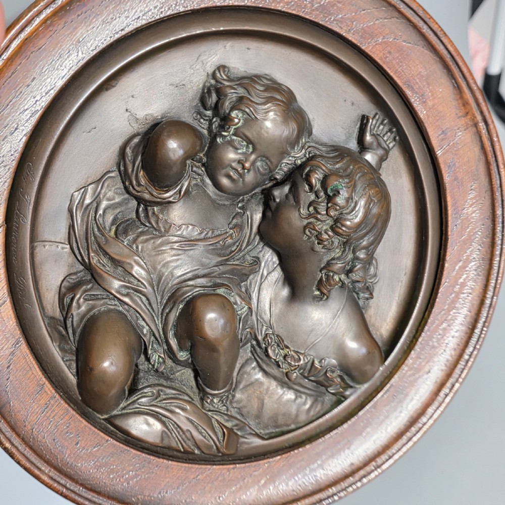 A circular Victorian bronze relief plaque depicting two young children in high relief, housed within a turned oak frame. View X
