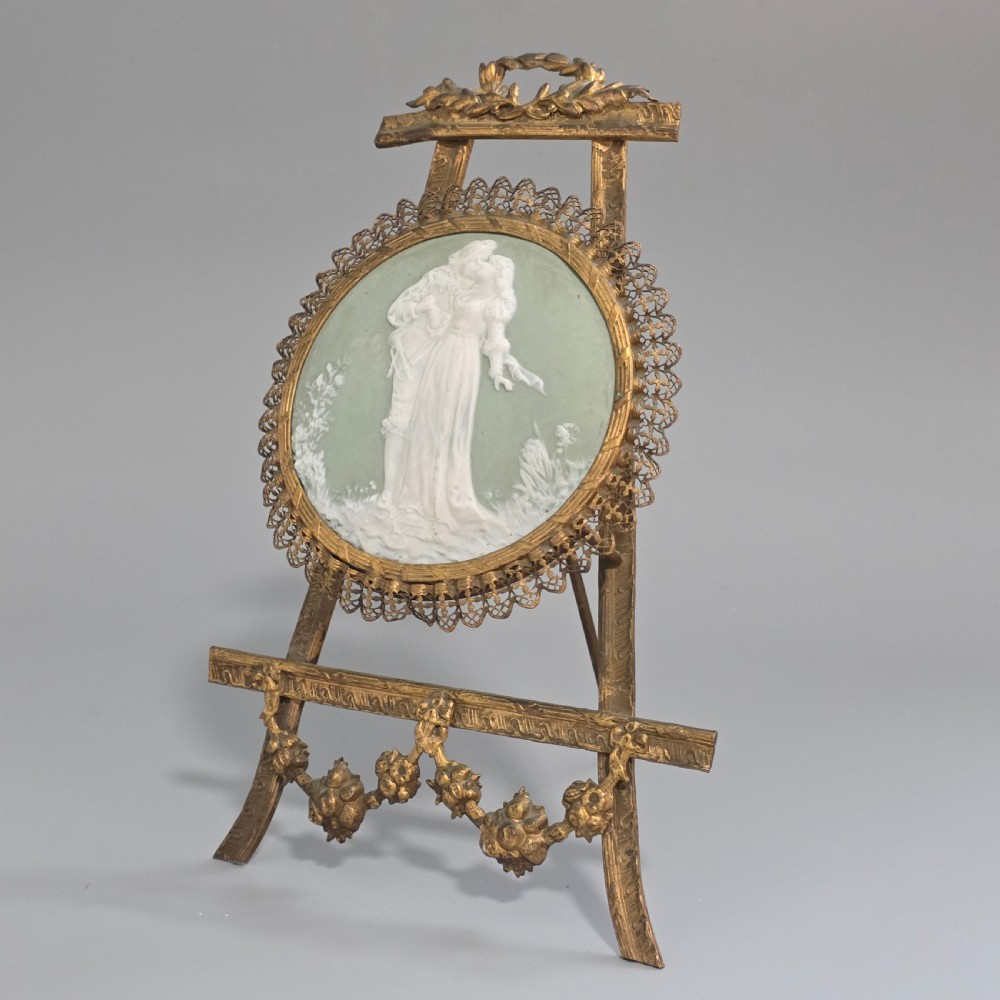 A pale green and white bisque porcelain oval plaque depicting two figures in high relief, supported on an ornate gilt metal easel. View II