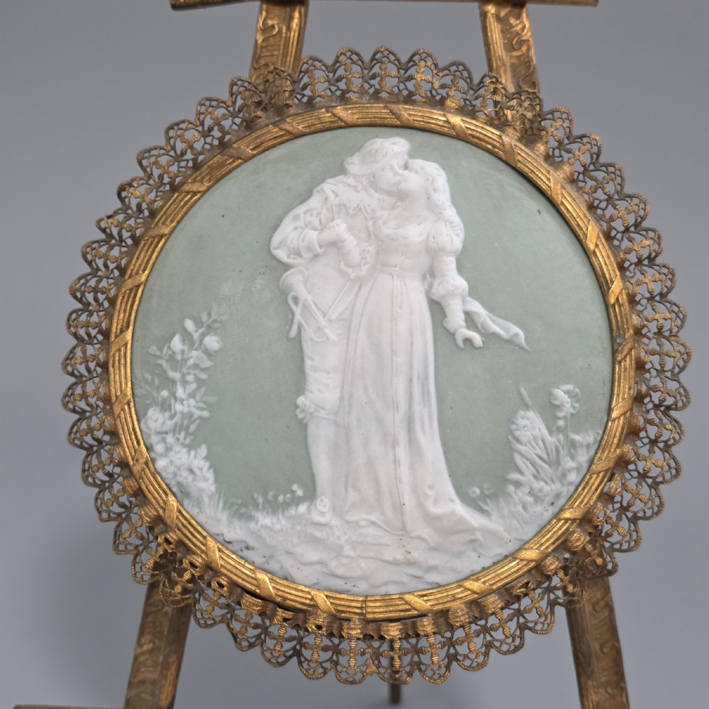 A pale green and white bisque porcelain oval plaque depicting two figures in high relief, supported on an ornate gilt metal easel. View VI
