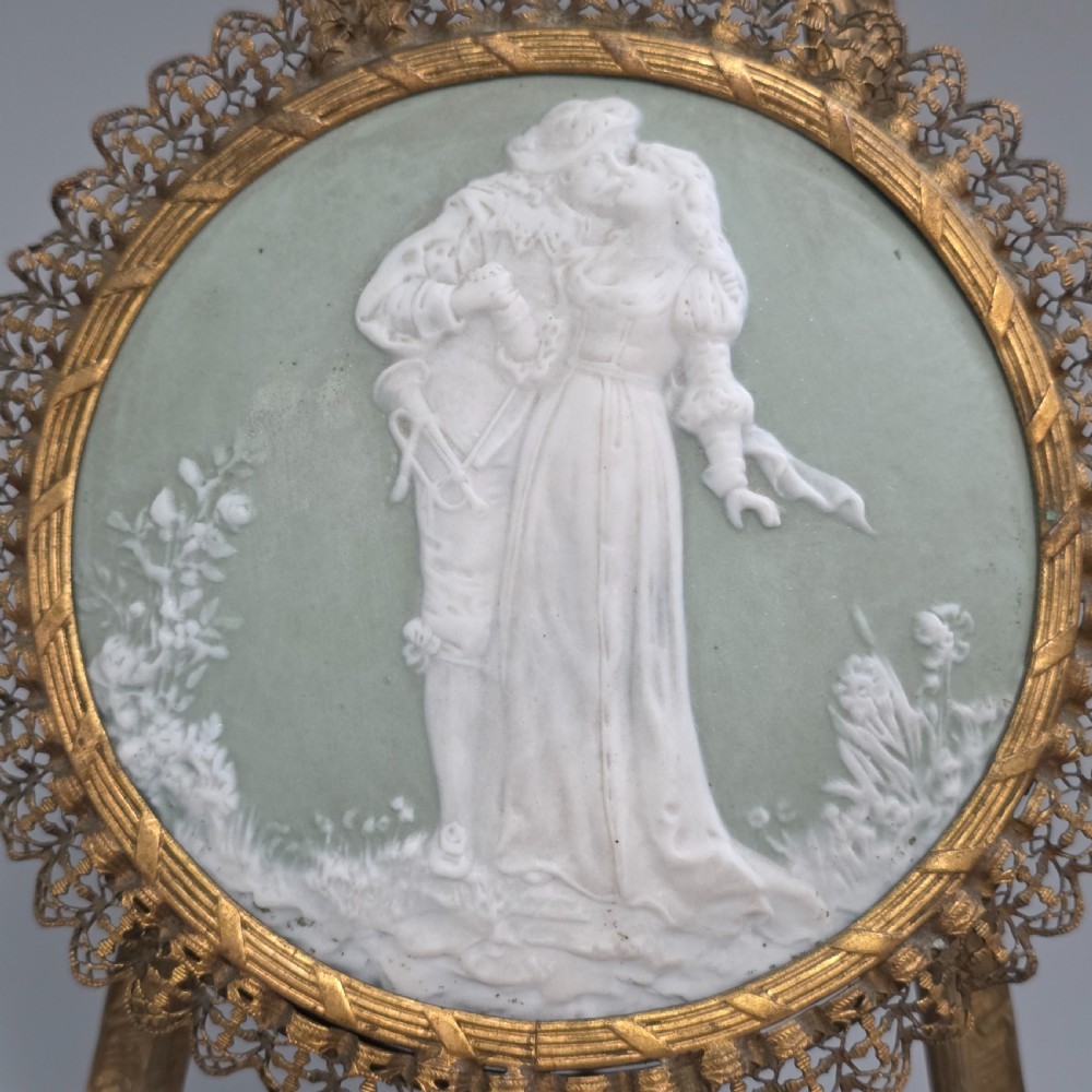 A pale green and white bisque porcelain oval plaque depicting two figures in high relief, supported on an ornate gilt metal easel. View VII