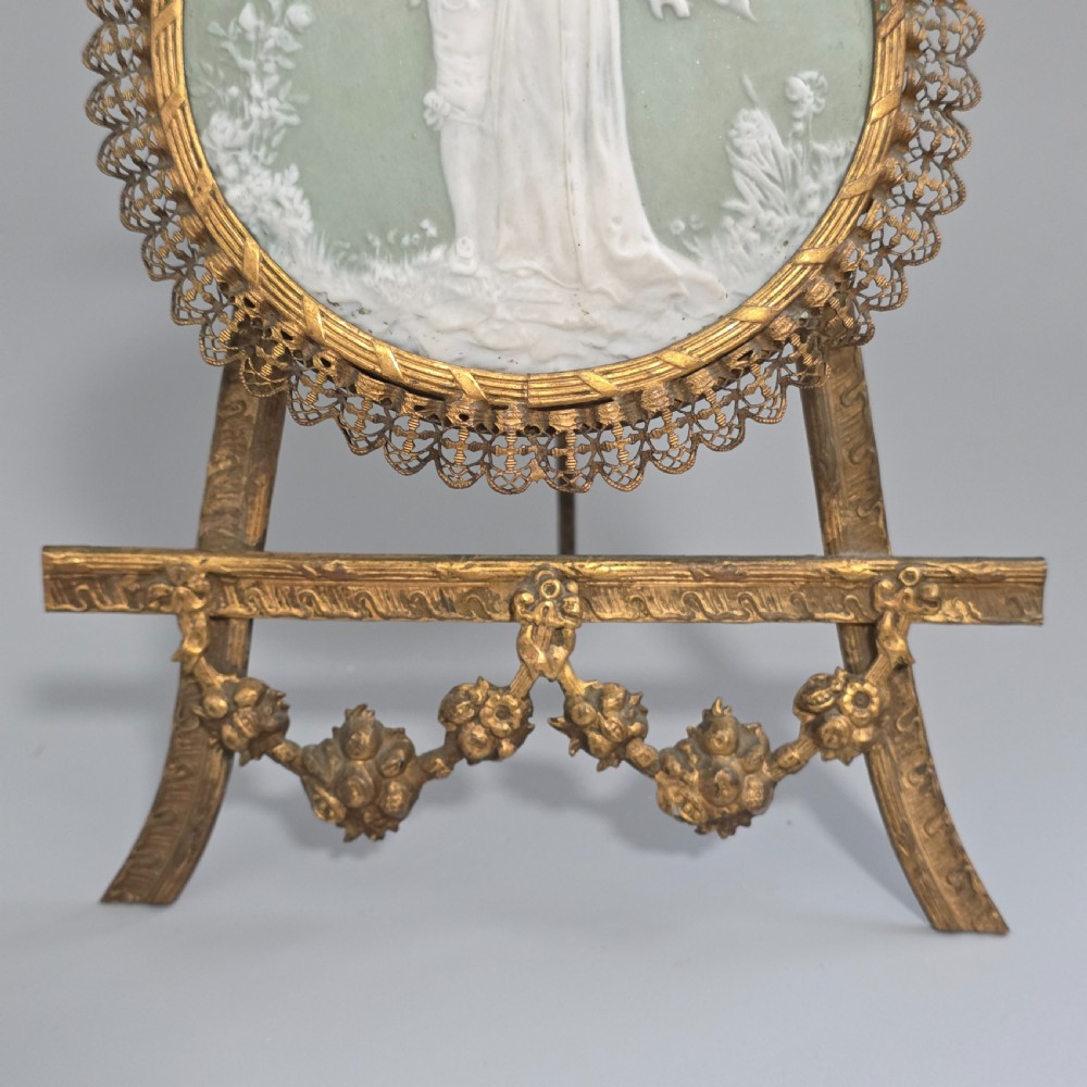 A pale green and white bisque porcelain oval plaque depicting two figures in high relief, supported on an ornate gilt metal easel. View VIII