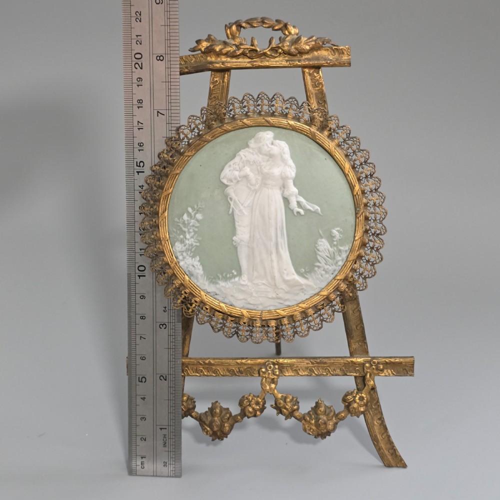 A pale green and white bisque porcelain oval plaque depicting two figures in high relief, supported on an ornate gilt metal easel. View XI
