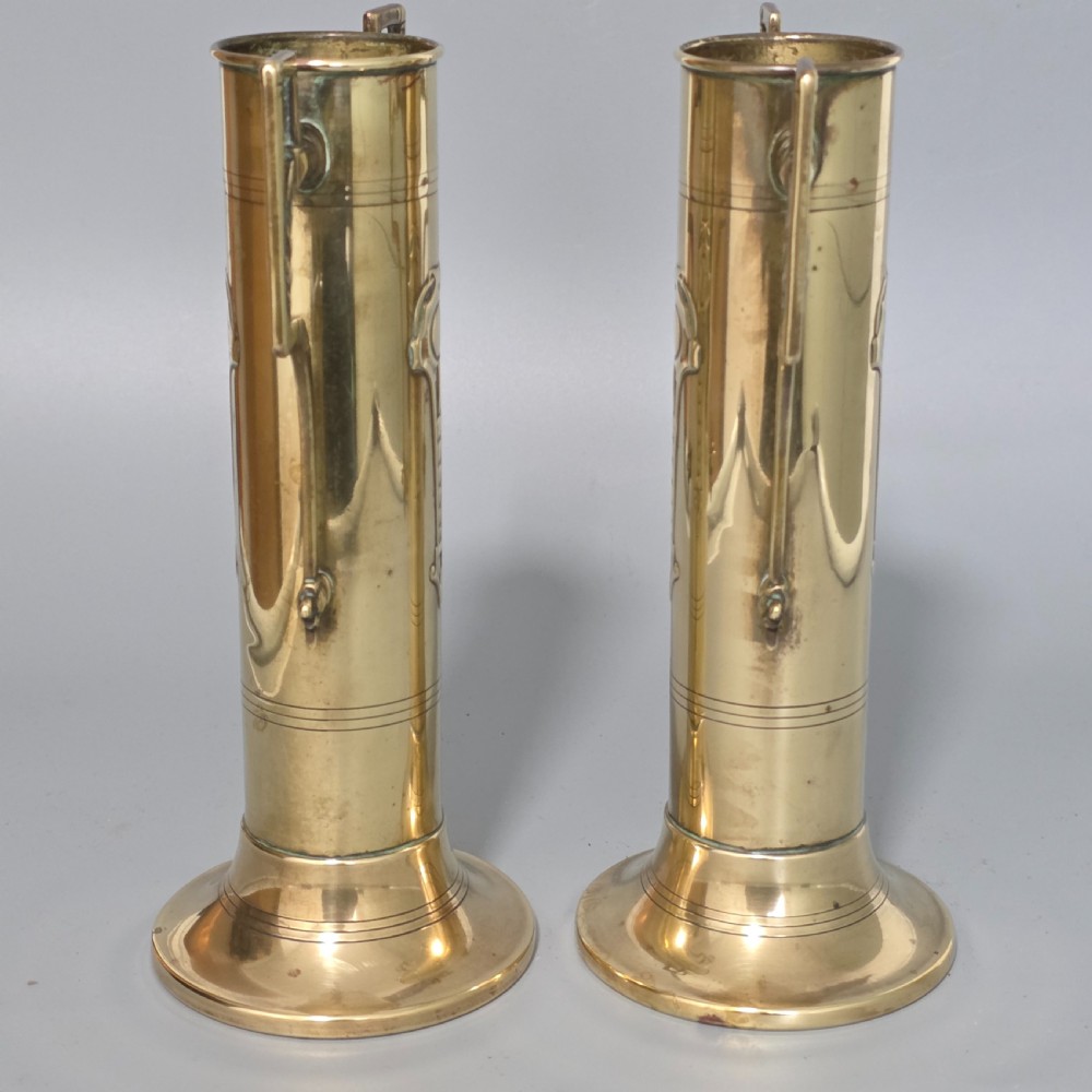 A pair of antique brass cylindrical vases featuring angular twin handles and raised stylised relief details on flared circular bases. View VIII