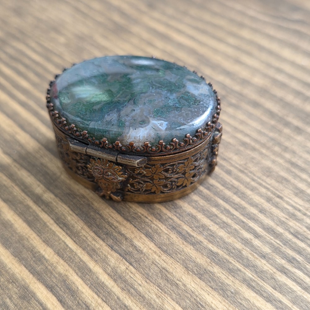 A small oval Victorian gilt metal pill box featuring a polished green moss agate cabochon lid and detailed relief scrollwork on the sides. View II