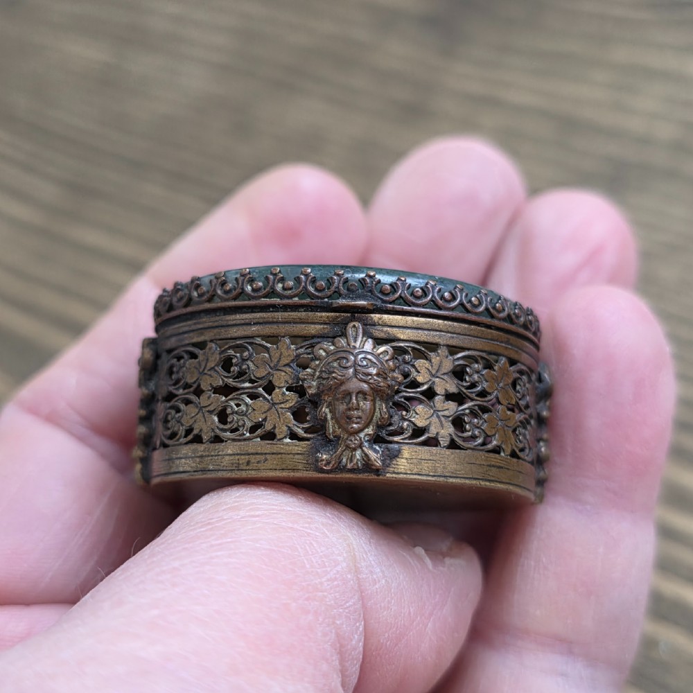 A small oval Victorian gilt metal pill box featuring a polished green moss agate cabochon lid and detailed relief scrollwork on the sides. View IV