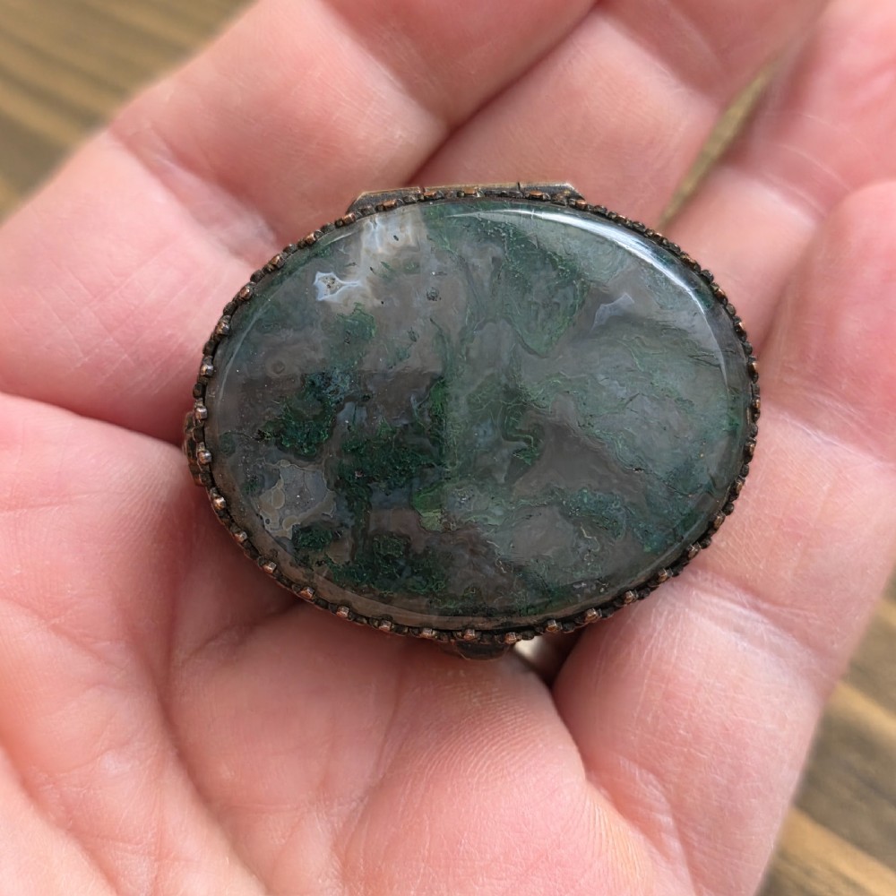 A small oval Victorian gilt metal pill box featuring a polished green moss agate cabochon lid and detailed relief scrollwork on the sides. View V