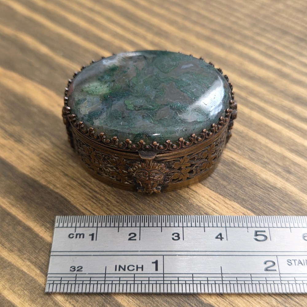 A small oval Victorian gilt metal pill box featuring a polished green moss agate cabochon lid and detailed relief scrollwork on the sides. View VIII