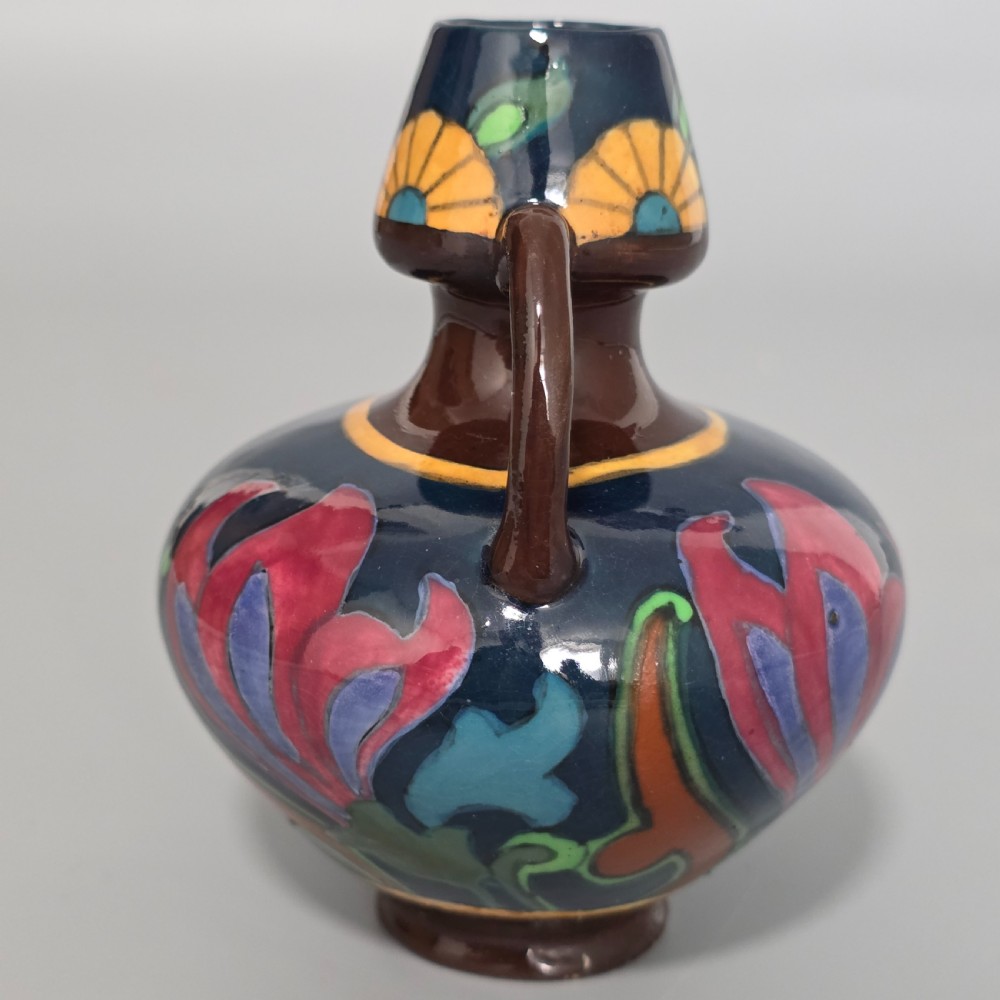 A glazed earthenware Art Nouveau vase with twin handles featuring a dark blue and brown ground decorated with stylised pink, purple, yellow, and green floral patterns. View II