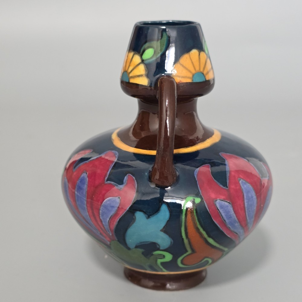 A glazed earthenware Art Nouveau vase with twin handles featuring a dark blue and brown ground decorated with stylised pink, purple, yellow, and green floral patterns. View III