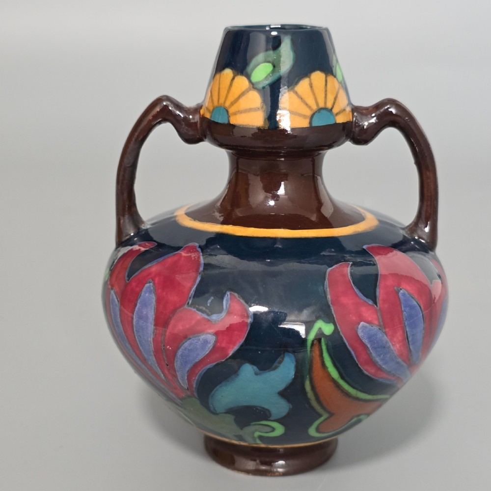 A glazed earthenware Art Nouveau vase with twin handles featuring a dark blue and brown ground decorated with stylised pink, purple, yellow, and green floral patterns. View IV