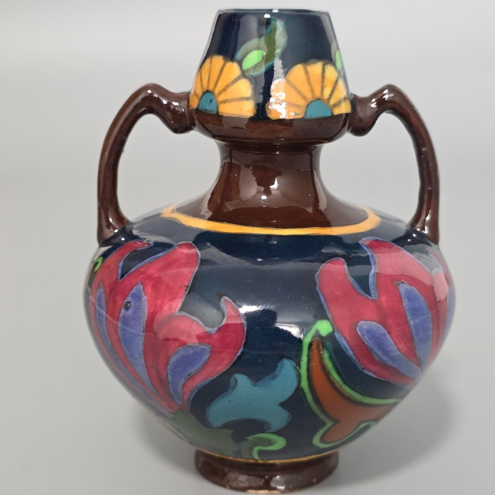 A glazed earthenware Art Nouveau vase with twin handles featuring a dark blue and brown ground decorated with stylised pink, purple, yellow, and green floral patterns. View V