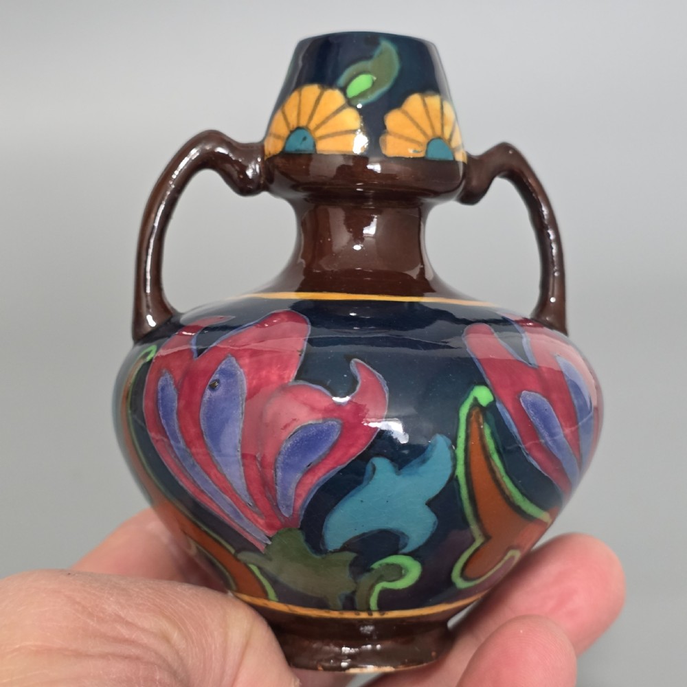 A glazed earthenware Art Nouveau vase with twin handles featuring a dark blue and brown ground decorated with stylised pink, purple, yellow, and green floral patterns. View VI