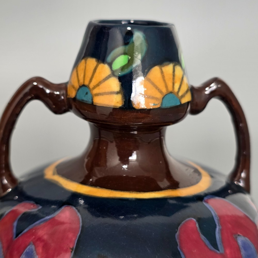 A glazed earthenware Art Nouveau vase with twin handles featuring a dark blue and brown ground decorated with stylised pink, purple, yellow, and green floral patterns. View VII