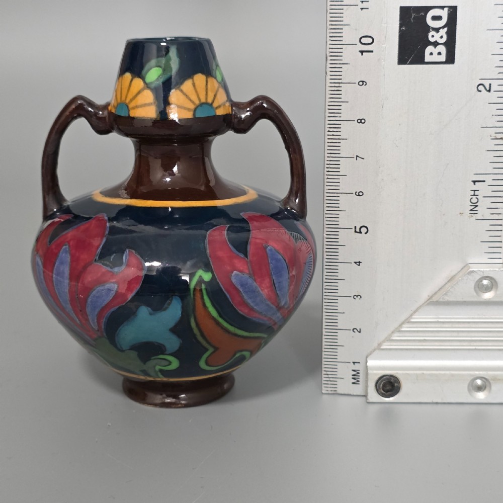 A glazed earthenware Art Nouveau vase with twin handles featuring a dark blue and brown ground decorated with stylised pink, purple, yellow, and green floral patterns. View XI
