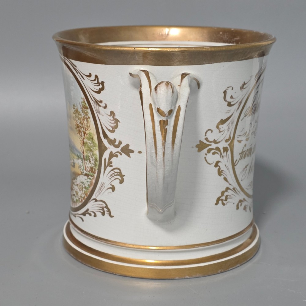 A nineteenth-century ceramic loving cup featuring two side handles, gilt trim, and a hand-painted landscape scene inside an oval cartouche. View II