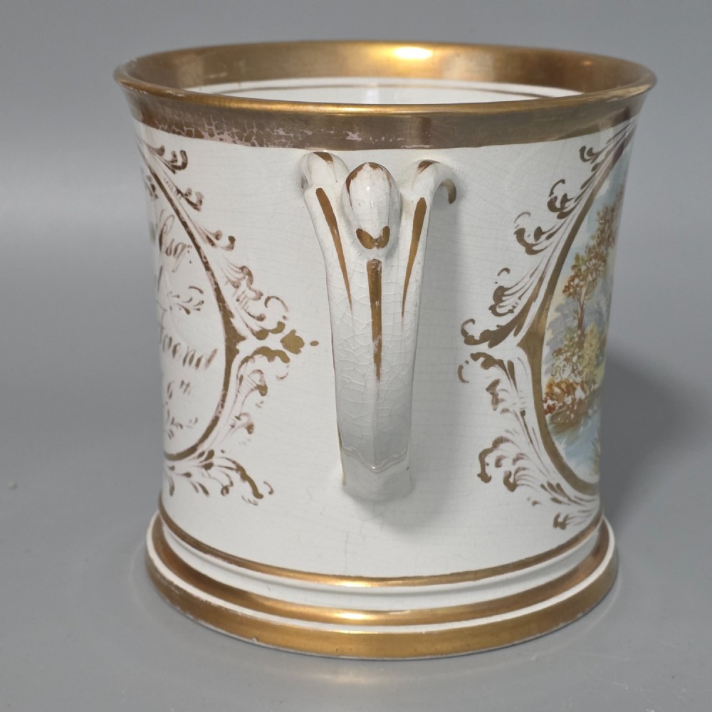A nineteenth-century ceramic loving cup featuring two side handles, gilt trim, and a hand-painted landscape scene inside an oval cartouche. View V