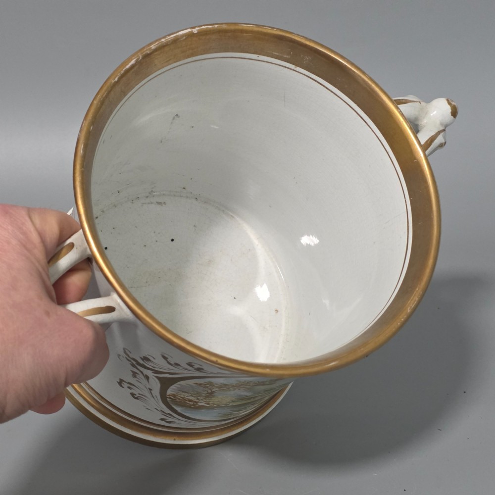 A nineteenth-century ceramic loving cup featuring two side handles, gilt trim, and a hand-painted landscape scene inside an oval cartouche. View VIII