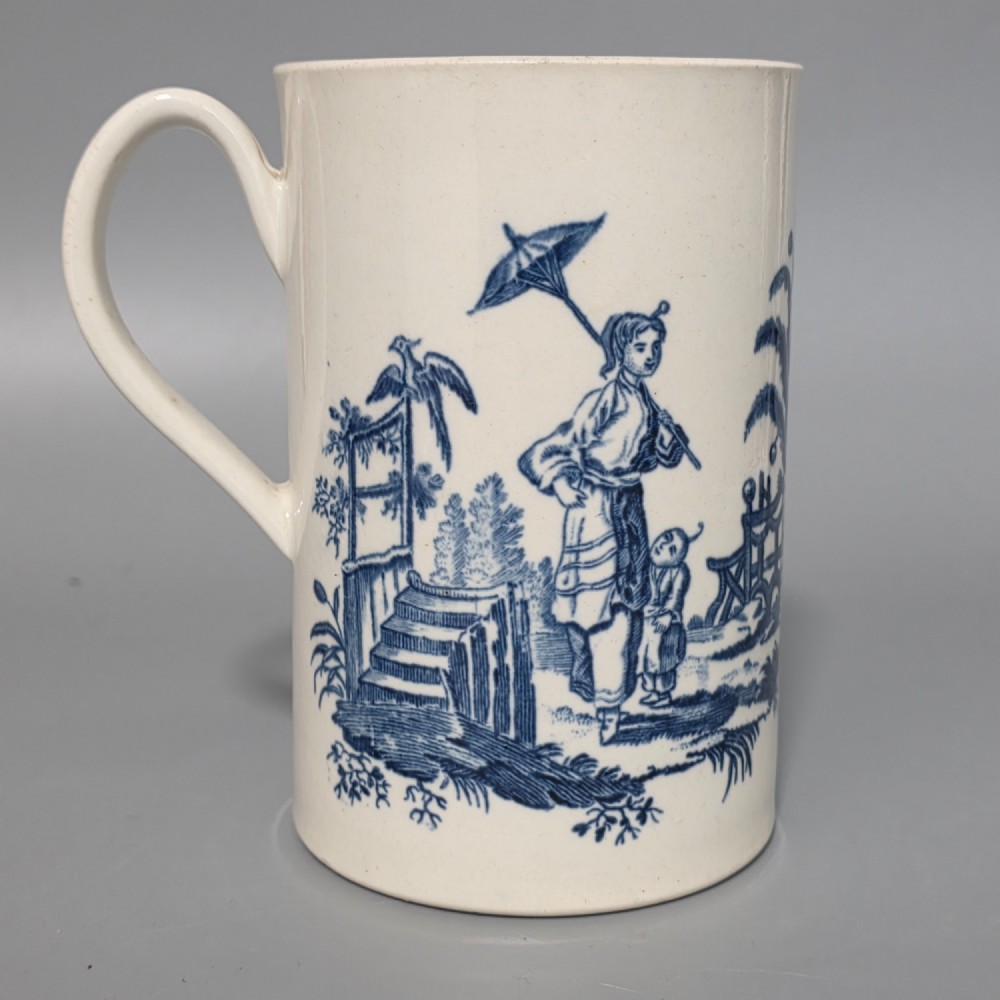 A tall cylindrical white porcelain mug featuring an 18th-century blue underglaze transfer-printed Chinoiserie design of figures and parasols with a single loop handle.