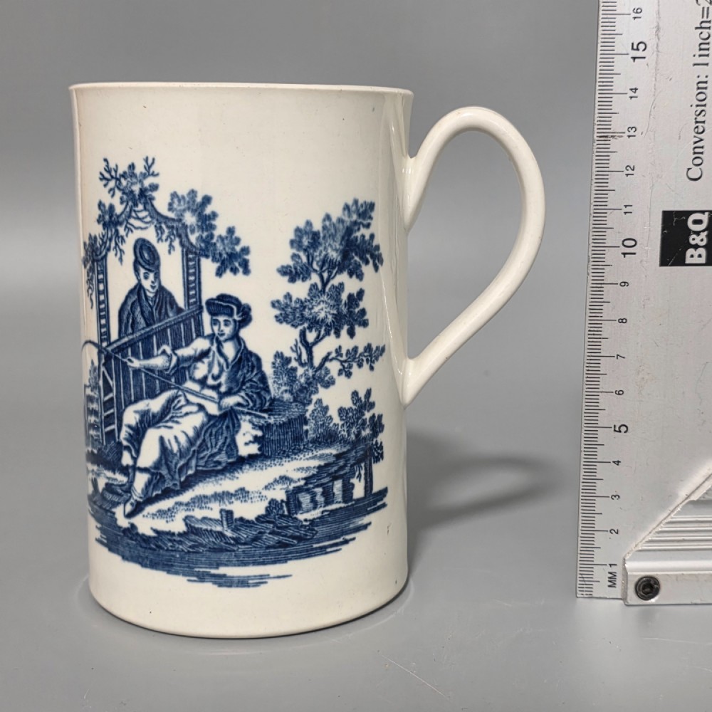 A tall cylindrical white porcelain mug featuring an 18th-century blue underglaze transfer-printed Chinoiserie design of figures and parasols with a single loop handle. View II