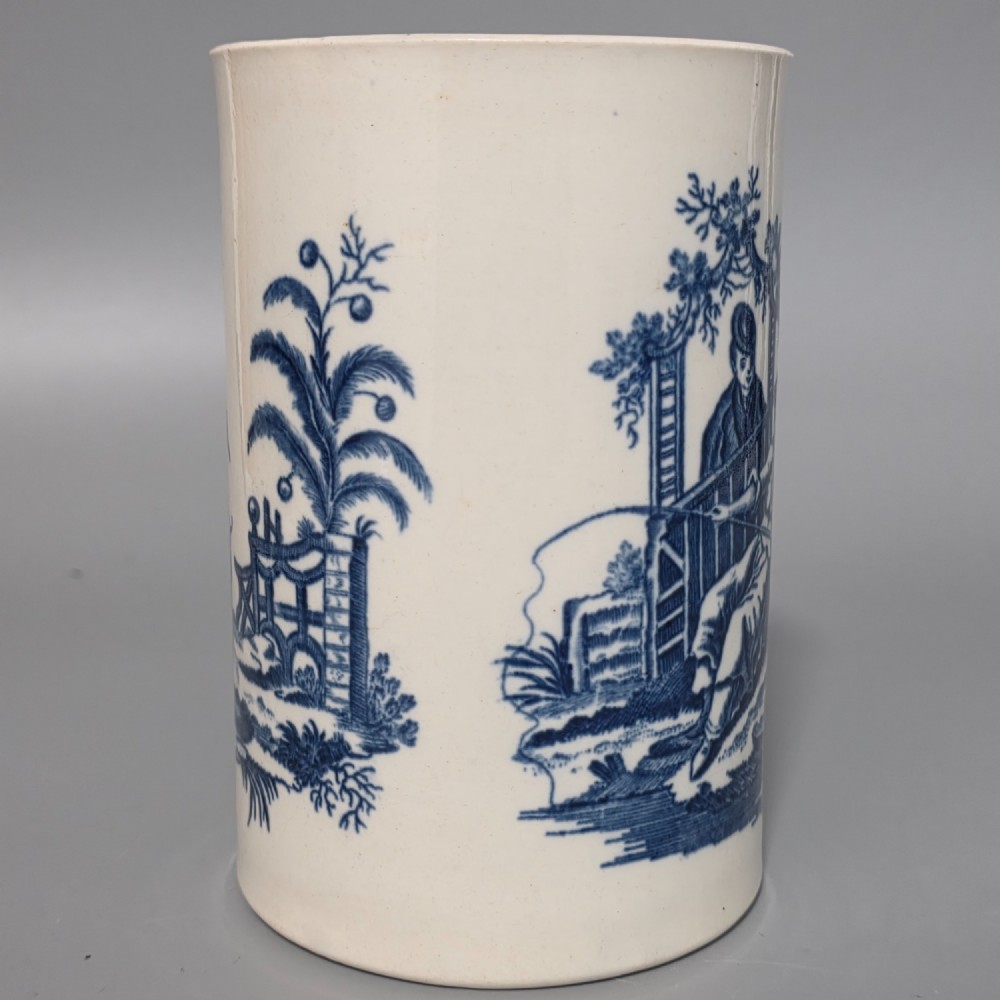 A tall cylindrical white porcelain mug featuring an 18th-century blue underglaze transfer-printed Chinoiserie design of figures and parasols with a single loop handle. View IV