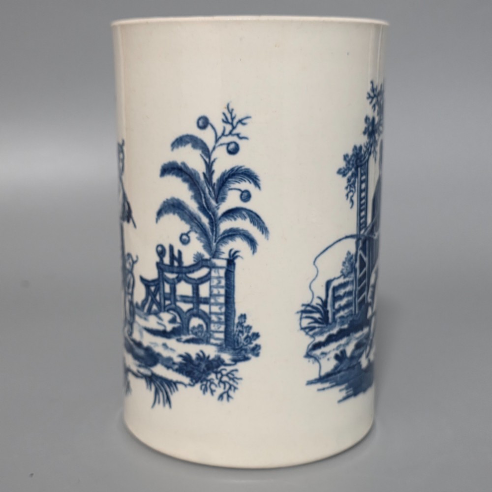 A tall cylindrical white porcelain mug featuring an 18th-century blue underglaze transfer-printed Chinoiserie design of figures and parasols with a single loop handle. View V