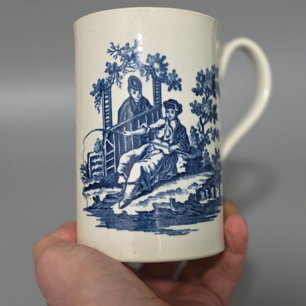 A tall cylindrical white porcelain mug featuring an 18th-century blue underglaze transfer-printed Chinoiserie design of figures and parasols with a single loop handle. View VII