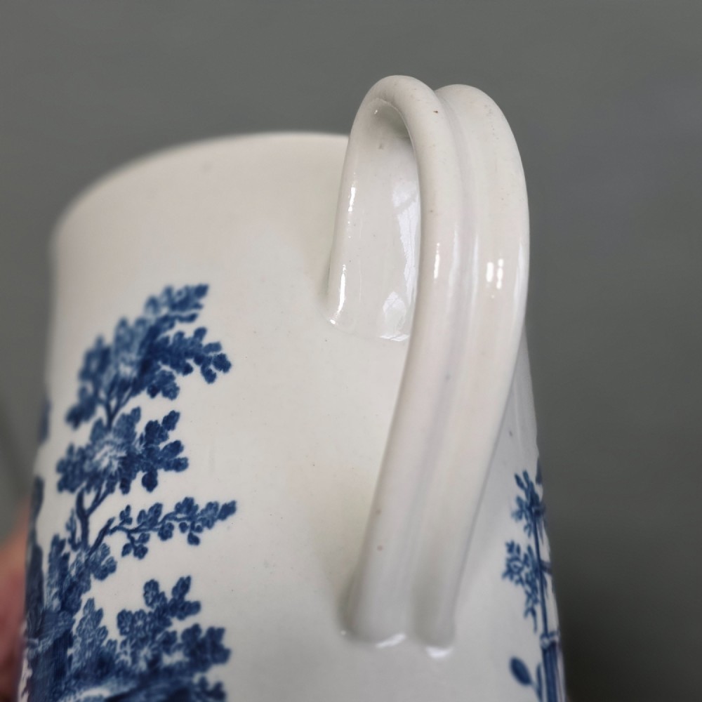 A tall cylindrical white porcelain mug featuring an 18th-century blue underglaze transfer-printed Chinoiserie design of figures and parasols with a single loop handle. View IX