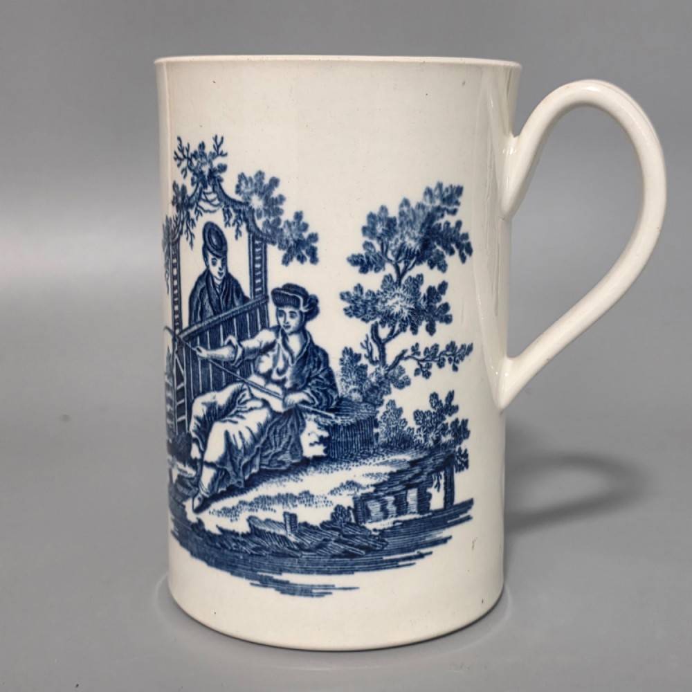 A tall cylindrical white porcelain mug featuring an 18th-century blue underglaze transfer-printed Chinoiserie design of figures and parasols with a single loop handle. View XIV