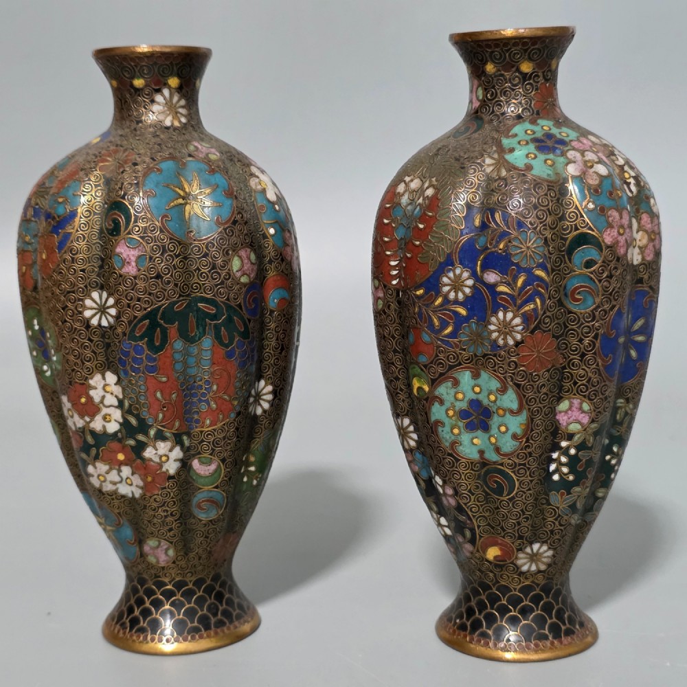 A pair of baluster-shaped Japanese cloisonne enamel vases decorated with intricate floral patterns, roundels, and scrollwork on a dark ground.